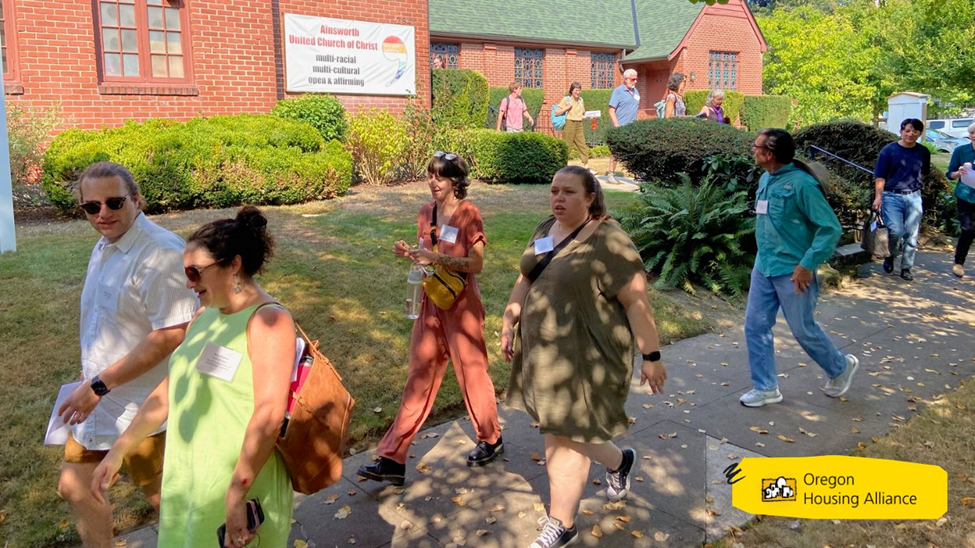 group of people walking in front of a church on a sunny day with dappled shadows from trees across them
